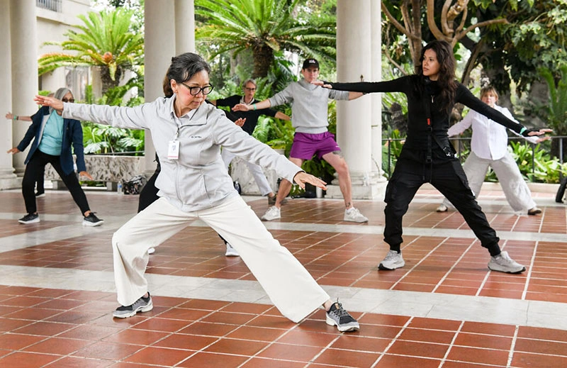 Kathy Chyan leads people in a tai chi pose on a loggia.