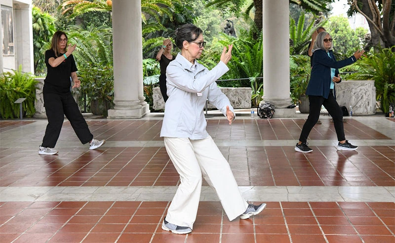 Kathy Chyan leads people in a tai chi pose on a loggia.