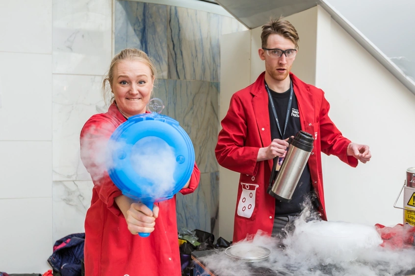 Two people in red lab coats make fog.