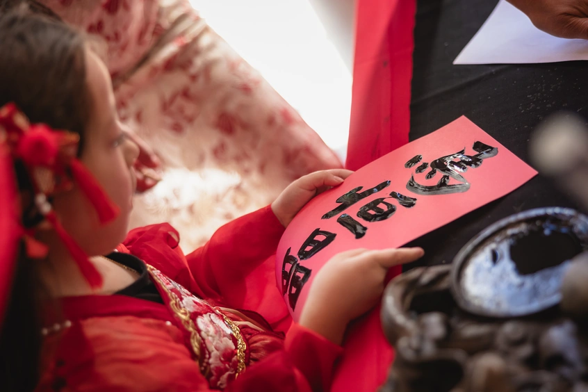 A child holds a red paper with Chinese characters painted in black ink.