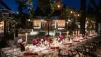 An outdoor courtyard is lit up at night while a long table set up for dinner service awaits guests.