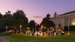 Tables, chairs, and heat lamps on a lawn with a beautiful sunset sky of blues and lavenders.