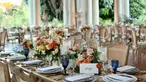 A table card sits among spring flower centerpieces on a long wooden table.