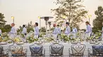 A lineup of wait staff in powder blue shirts and white aprons hold appetizers and plates.