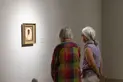 Two people look at a painting on a wall.