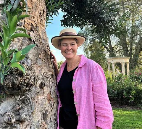 Nicole poses for the camera standing next to a tall tree in the Huntington Rose Garden.