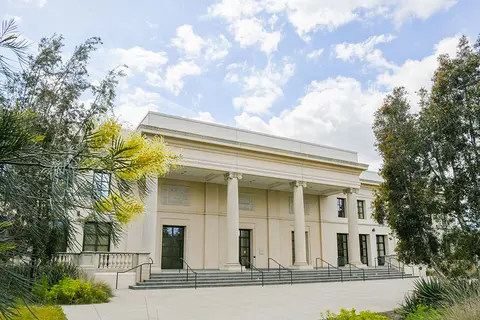 A small set of stairs lead up to a two story building with a 4-column portico.