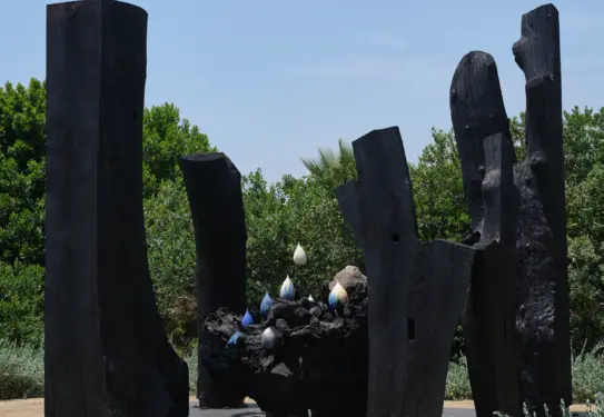 A large sculpture in a garden, created with charred wood and ceramics.