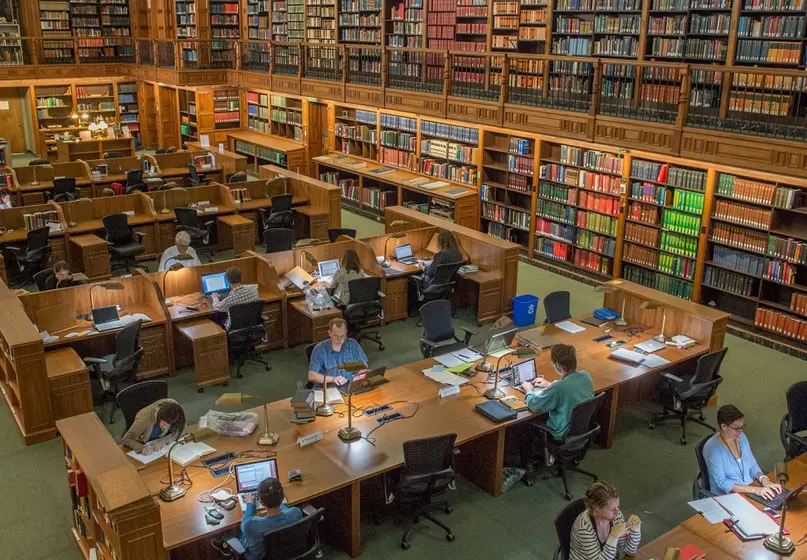 A large two-story room with book-lined walls and long tables, where people work.