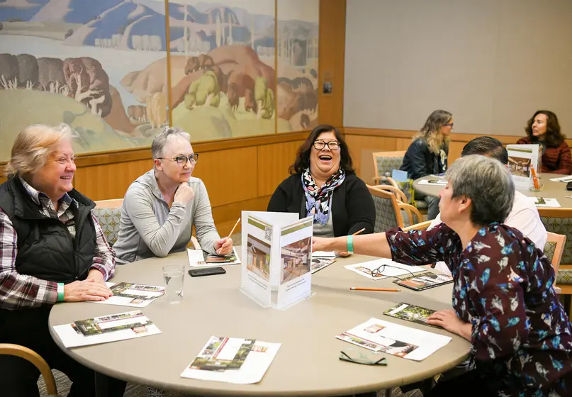 A group of people sit and interact a circular table.