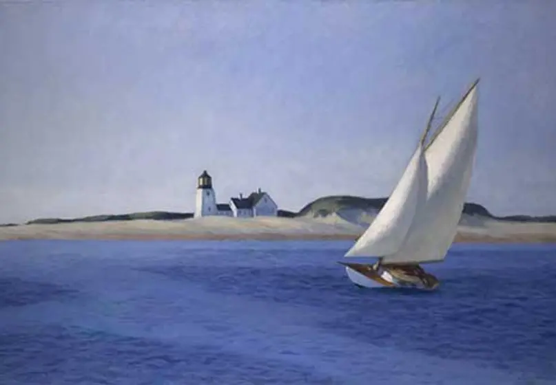 A leaning sailboat sits in calm deep-blue waters not far from a sandy beach and lighthouse.