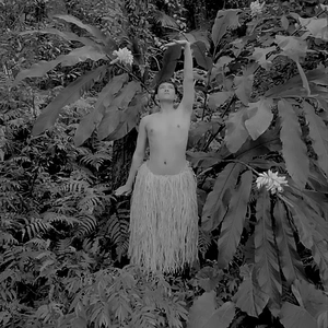 A person in a grass skirt stretches in a forest.