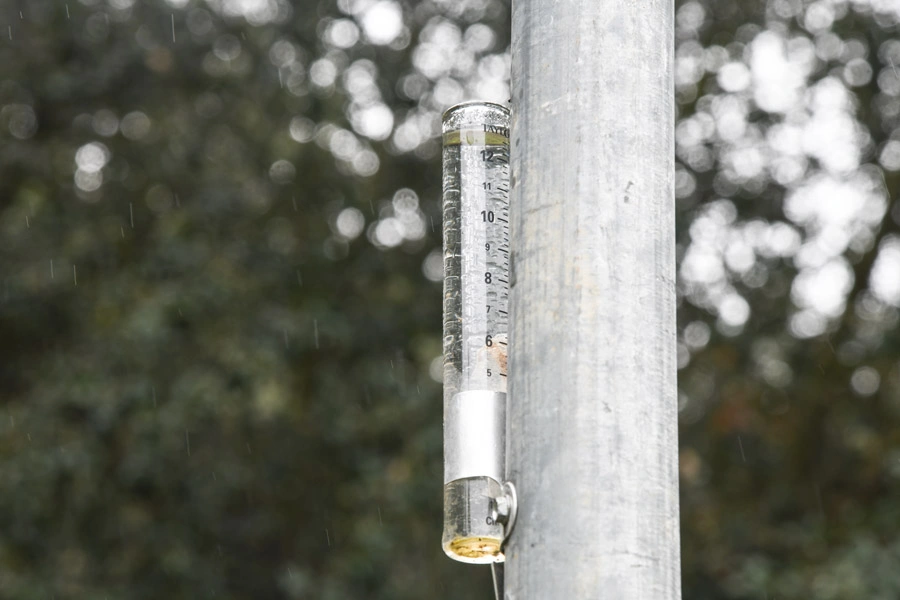 A rain gauge attached to a metal pole.