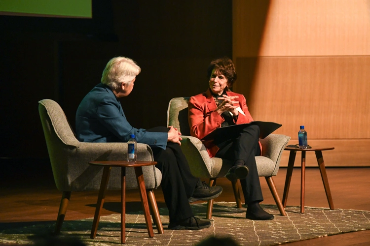 Two people sit in chairs on a stage.