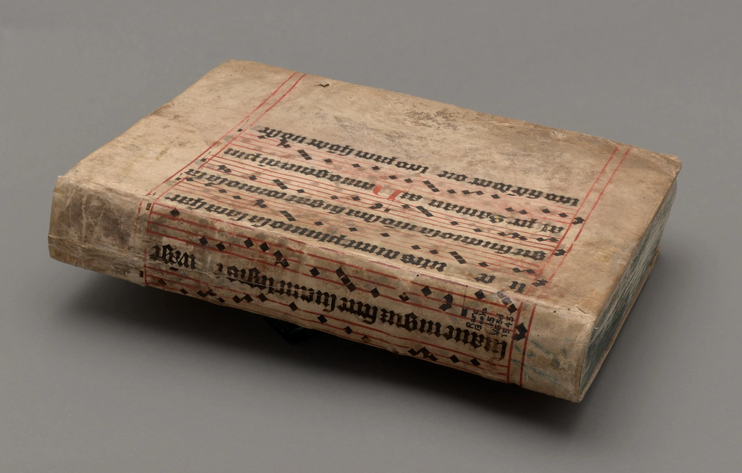 A bound book featuring a musical composition in black ink on red lines.