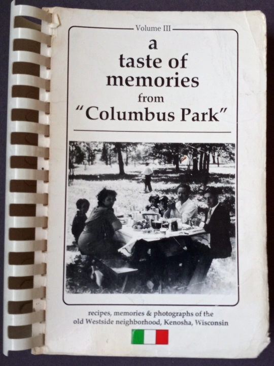 A cookbook cover with a black-and-white photo of people at a table in a park and the title “A Taste of Memories from ‘Columbus Park.’”