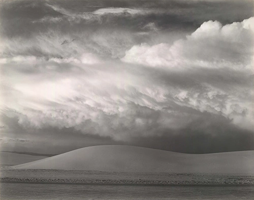 A white sand dune with clouds above.