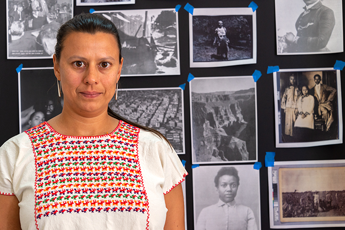 Carolina Caycedo stands in front of the presentation screens on which she has arranged black-and-white photographic copies gathered from her research. Photo by Kate Lain.