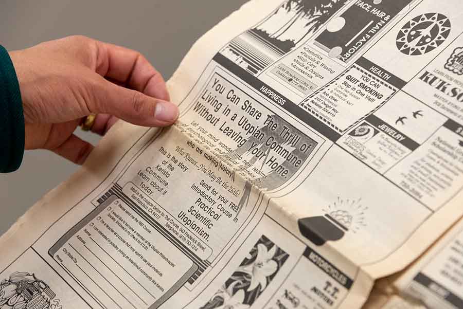 Woo reads an advertisement for a utopian commune in a newspaper from the Robert Hine Collection. Photo by Kate Lain.